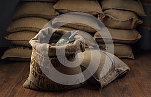 Open bag full of raw coffee beans with metal scoop, in the background of the warehouse