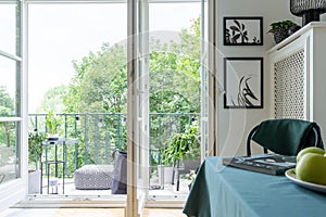 Open balcony door with a view of trees. Pouf and table on a balcony