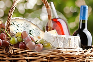 open basket with organic cheeses and grapes, wine bottle beside