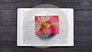 Open Bible. Book. Gift in a red package with a gold bow. On a wooden table.