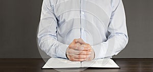 Open Bible book on the table. Prayer. White cup. Young man in shirt prays with folded hands.