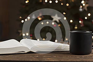 Open Bible book on a wooden table. A cup of coffee. Against the background of the Christmas tree