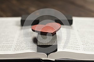 Open Bible book on a wooden table. Wooden cross of Jesus. Red heart. The concept of loving God`s Word