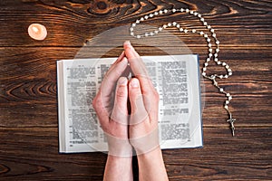 Open bible, candle, christian cross and human hands on wooden background. Prayer to God