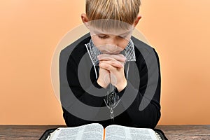 An open Bible in front of a praying child with folded hands