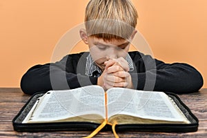 An open Bible in front of a praying child with folded hands