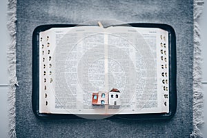 Open Bible on a light background with a miniature church. Online service concept