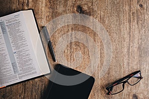 Open Bible and notebook on a wooden desk. Top view flat lay