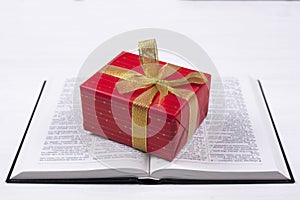 An open Bible on the table. A gift on a book. A red gift-wrapped box with a gold bow. A gift from God
