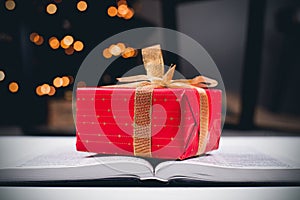 An open Bible on the table. A gift on a book. A red gift-wrapped box with a gold bow. A gift from God