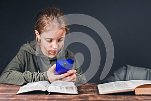 An open Bible on the table. A girl with a phone in her hands. Ignores books and plays video games on phone.