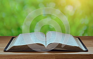 Open Bible on a wood table with green nature backgound