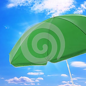 Open big green beach umbrella and beautiful blue sky with white clouds on background