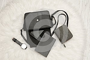 Open black bag with dropped things, notebook, mobile phone, watch and gray purse. The white fur on background, top view.