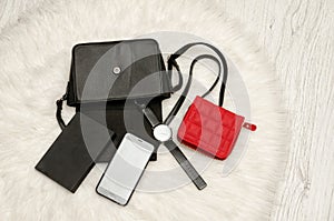 Open black bag with dropped things, notebook, mobile phone, watch and red purse. The white fur on background, top view.