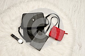 Open black bag with dropped things, notebook, mobile phone, watch and red purse. The white fur on background, top view.