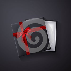 Open black empty gift box with red bow and ribbon on dark background. Top view. Template for your presentation, banner or poster.