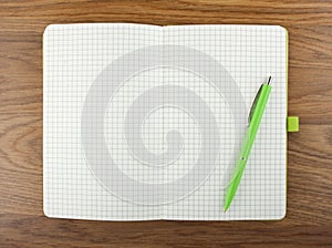 Open blank checked notebook with green pen on a table.