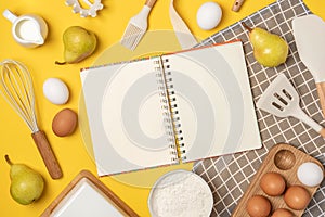 Open blank notebook, baking ingredients and cooking utensil, on yellow backgroun. Template for cooking recipes or your design. Top