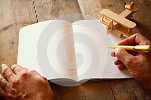 Open blank notebook and man hands next to toy aeroplane on wooden table. retro style filtered image