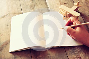 Open blank notebook and man hands next to toy aeroplane on wooden table. retro style filtered image