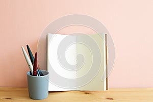 Open blank notebook and pen on wooden desk. Pink background