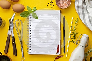 Open blank notebook for recipes, yellow background, food ingredients and utensils for cooking. Copy space.
