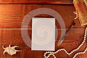 Open a blank notepad in a center, pen, sea shell and pearl necklace on a red textured wooden table. Concept of setting goal for ne