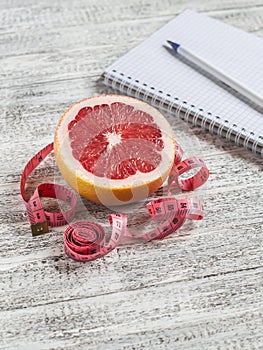 Open a blank Notepad, grapefruit and measuring tape on a light wooden table. The concept of healthy nutrition, diets