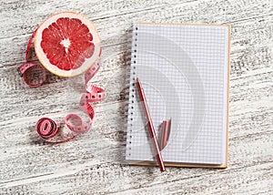 Open a blank Notepad, grapefruit and measuring tape on a light wooden table. The concept of healthy nutrition, diets, healthy life