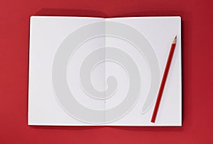 Open blank notepad and red pencil on a red background, with copy space