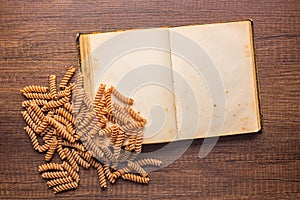 Open blank recipe book and raw whole grain fusilli pasta on wooden table. Top view