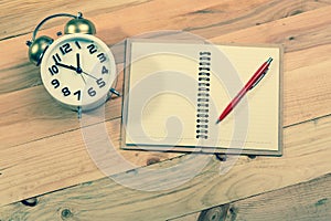 Open a blank white notebook, pen and alarm clock