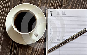 Open a blank white notebook, pen and cup of coffee on the wooden desk