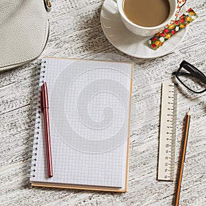 Open a blank white notebook, pen, women's bag, ruler, pencil and cup of coffee