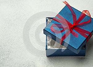 Open blue box with a gift and a red ribbon on a light background with place for text