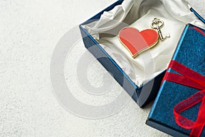 Open blue box with a gift and a red ribbon on a light background with place for text with red heart and key