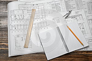 Open blueprints on wooden table background with a pencil, a ruler and compasses lying beside.