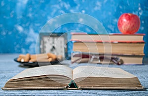 An open book on the background of a stack of books and an apple