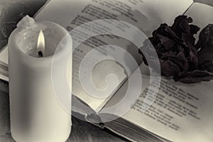 An open book with a candle. on the pages is a Bud of dried rose.