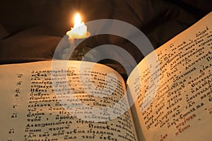 Open book with candle soft light pouring on text. Reading of ope