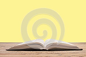 open book. Composition with hardback books, fanned pages on wooden deck table and yellow background. Books stacking. Back to