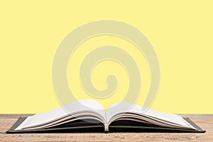 open book. Composition with hardback books, fanned pages on wooden deck table and yellow background. Books stacking. Back to