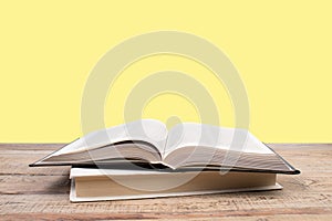 open book. Composition with hardback books, fanned pages on wooden deck table and yellow background. Books stacking. Back to