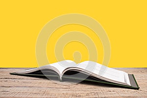 open book. Composition with hardback books, fanned pages on wooden deck table and yellow background. Books stacking. Back to