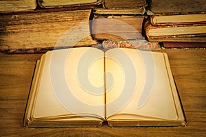 Open book with empty pages on a wooden table in front of a pile of old weathered books