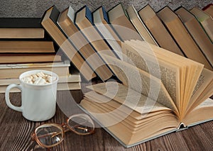 An open book, glasses, a cup of cocoa with a marshmallow close - up on a wooden background.