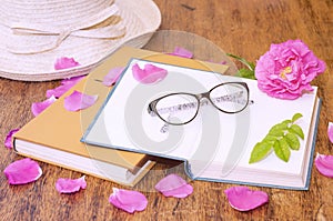 Open book, glasses for reading and rosehip flower petals on a wooden table