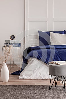 Open book on grey pouf in trendy bedroom interior with blue and white design