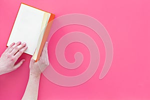 Open the book. Hands hold hardback book opened on pink background top view copy space